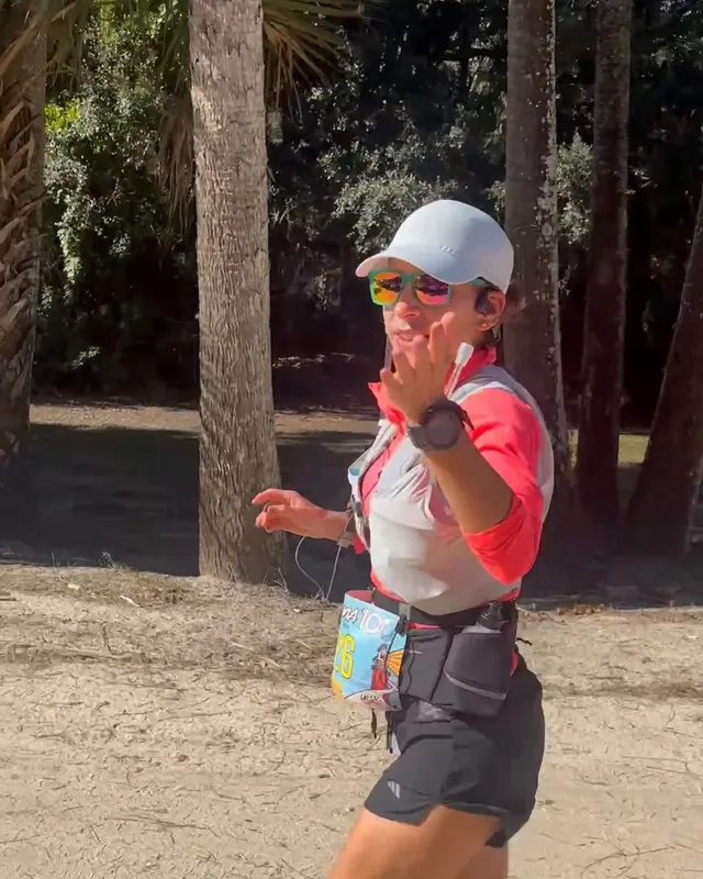 Mónica corre por un camino de arena entre palmeras y saluda a la cámara.