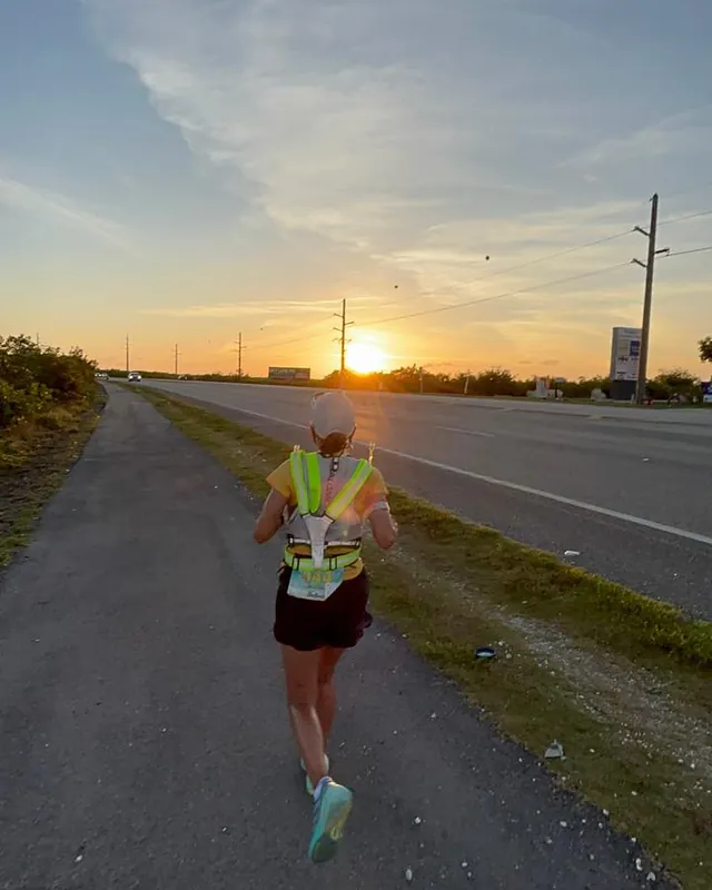 Al atardecer, Mónica corre por el sendero junto a la carretera, hacia el sol.